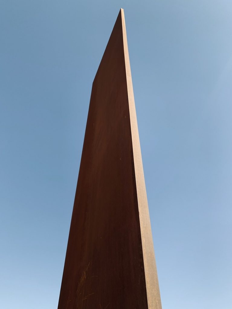 Oxidized steel plate of East-West/West-East Sculpture by Richard Serra against clear blue sky.