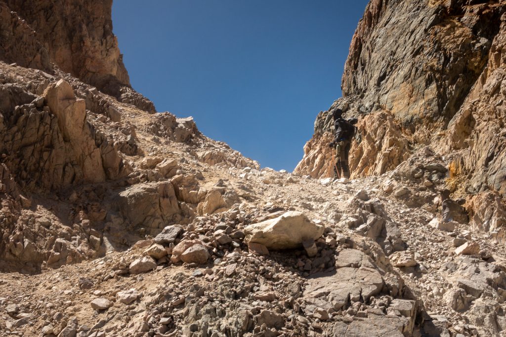 A hiker going through the crumbling rocks found on the Piuquenes Pass trail