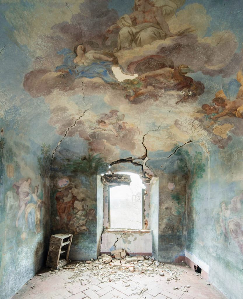 Resilient Sky by Nicola Bertellotti. A large crack comes from the window of a decaying room covered in forgotten murals of angels and religious figures.