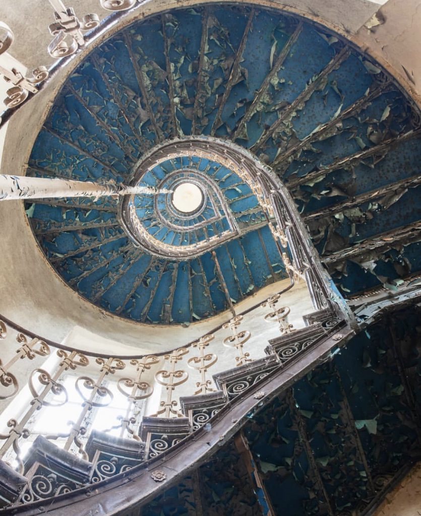 Le Grand Bleu by Nicola Bertellotti. Looking up through the swirl of a peeling blue staircase into the light of the ceiling. 